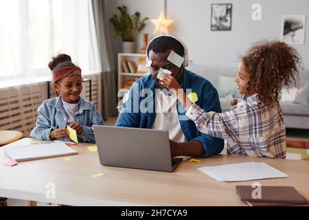 Portrait of two children playing with father trying to work from home, copy space Stock Photo