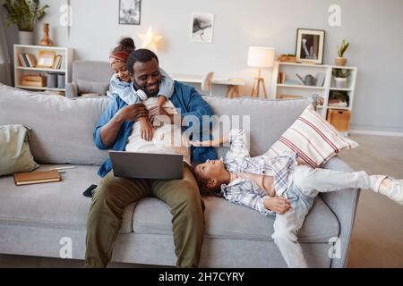 Portrait of happy African-American father playing with two cute daughters and using laptop, copy space Stock Photo