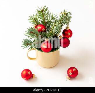 Christmas fresh fir twigs and red baubles decoration in an enamel cup isolated on white background. Merry Xmas New Year greeting card Stock Photo