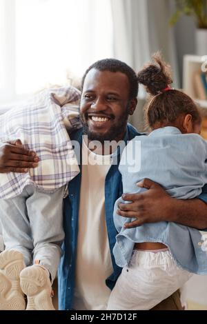 Vertical portrait of happy African-American father having fun with two cute daughters at home Stock Photo