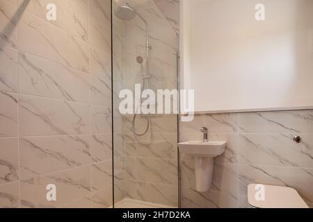 Generic home shower room with basin and wc partially tiled walls and glass shower screen. Stock Photo
