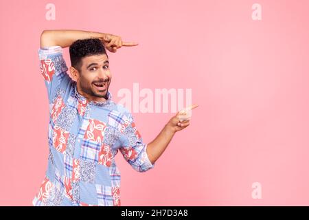 Wow, attention to advertising. Portrait of happy bearded man pointing to side copy space with both hands and showing blank wall for idea presentation. Indoor studio shot isolated on pink background. Stock Photo