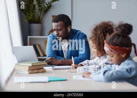 Portrait of caring father doing homework with two little girls in online school at home, copy space Stock Photo