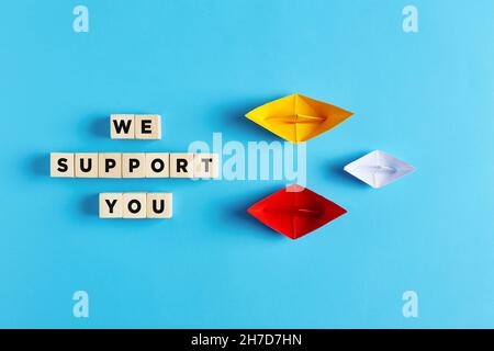 Two paper boats support the small boat with the we support you text. Assistance, consultancy, aid or support service in business or technology concept Stock Photo