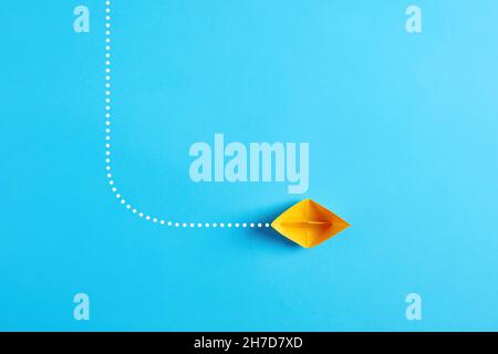 Choosing the new, right or alternative change path in business concept. Yellow paper boat makes a turn and changes direction on blue background. Stock Photo