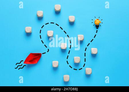To overcome obstacles and to find a creative idea in business or education concept. Red paper boat finds a way to reach the light bulb by passing thro Stock Photo
