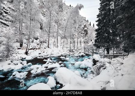 Beautiful landscape of blue water river and Spruce tree forest in the mountains with snow at winter time Stock Photo
