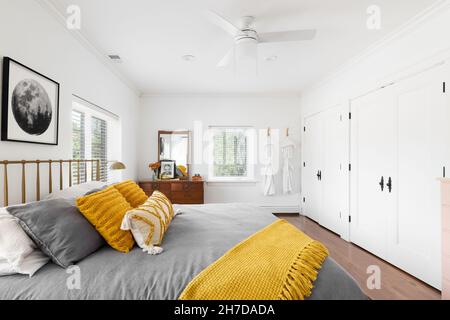 A bright bedroom with white walls, yellow and grey bedding, and a rug on hardwood floors. Stock Photo