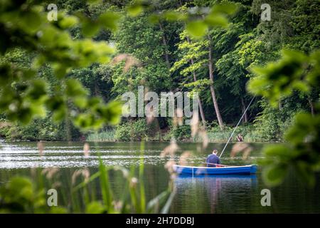 a fisherman fishing from a rowboat on a lake Stock Photo
