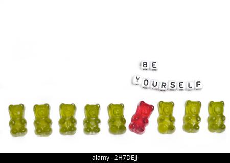 a row of green gummy bears in which a red guy behaves differently out of a concept for individuality and being different is isolated on a white backgr Stock Photo
