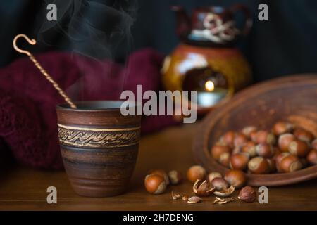 Dark background with a hot drink in a ceramic Cup and the scattered nuts hazelnuts on a wooden surface. Stock Photo