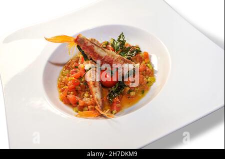 Goatfish or Red mullet in tomato sauce with parsley in white plate . Italian fish recipe called Triglie alla livornese. Isolated on white Stock Photo