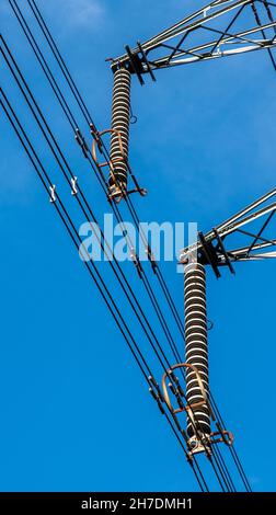 Two electrical insulators with power cables on a pylon with blue sky background. Stock Photo