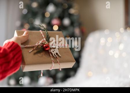 Christmas eco gift in woman hands. Glowing snow bokeh, fir tree. Winter holidays mock up on white background. Zero waste, plastic free. Stock Photo