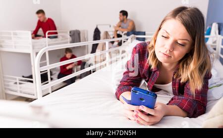 Girl with phone lying on bed in hostel Stock Photo