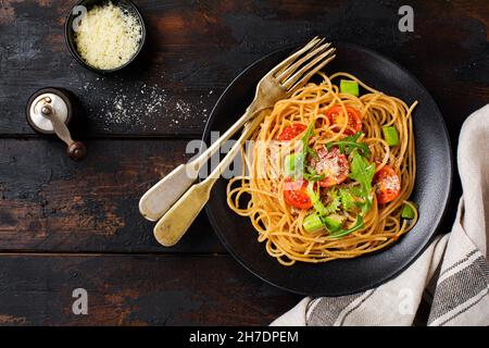 Spaghetti pasta with pesto, avocado and tomatoes in rustic white plate. Raw vegan food concept. Top view. Stock Photo