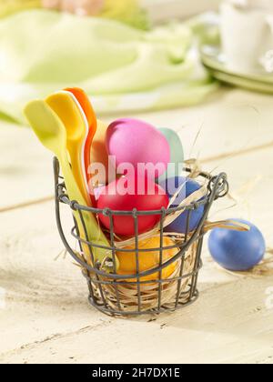 Colourful Easter eggs and plastic spoons in a wire basket lined with straw Stock Photo