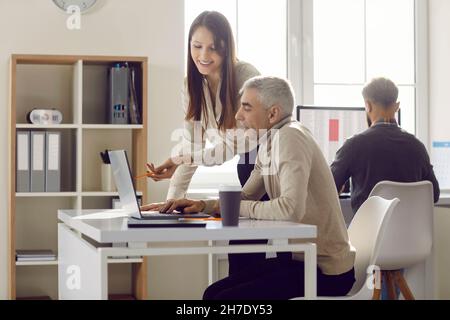 Young employee discusses online project, showing computer presentation to senior team leader. Stock Photo