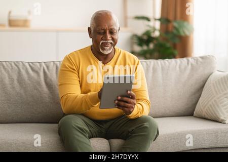 Senior Black Man Using Tablet Browsing Internet Sitting At Home Stock Photo