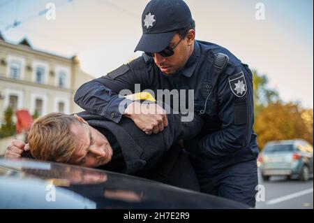 Police officer in sunglasses arrests young man Stock Photo