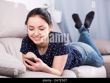 Happy woman on sofa with smartphone Stock Photo