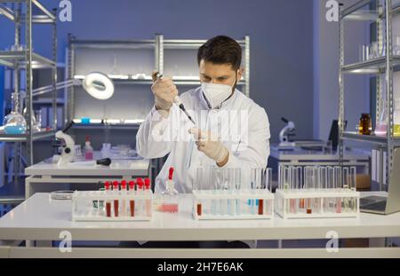 Serious cautious man scientist with pipette adds liquid to test tube in medical laboratory. Stock Photo