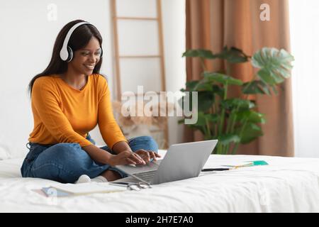 Happy African American Female Using Laptop Wearing Earphones At Home Stock Photo