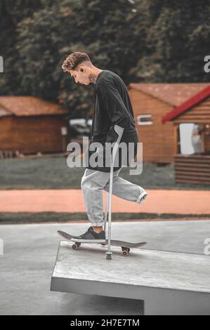 Guy with crutches on skateboard on springboard in park Stock Photo