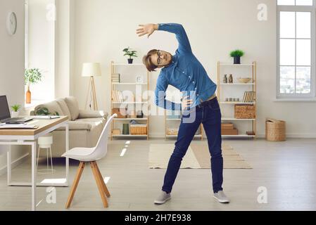 Young man doing stretching exercise while having fitness workout at work or at home Stock Photo