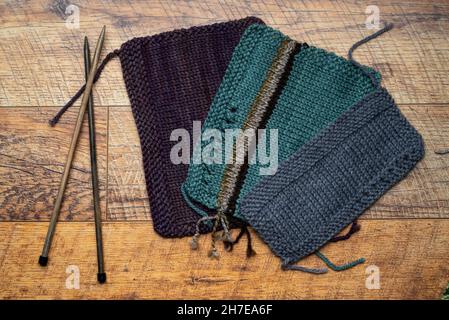 Top view of knitted swatches yarns, needles on brown wooden background. Stock Photo