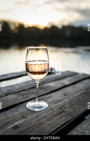 Sunset view of a glass of orange wine on a wooden pier on a lake. Wine drinking on a beautiful location Stock Photo