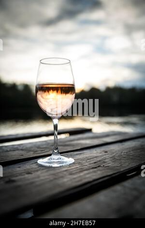 Sunset view of a glass of orange wine on a wooden pier on a lake. Wine drinking on a beautiful location Stock Photo