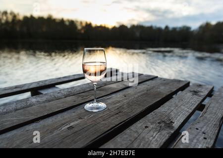 Sunset view of a glass of orange wine on a wooden pier on a lake. Wine drinking on a beautiful location Stock Photo