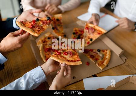 Colleagues Taking Pizza Slices From Box During Lunch Break In Office, Closeup Stock Photo