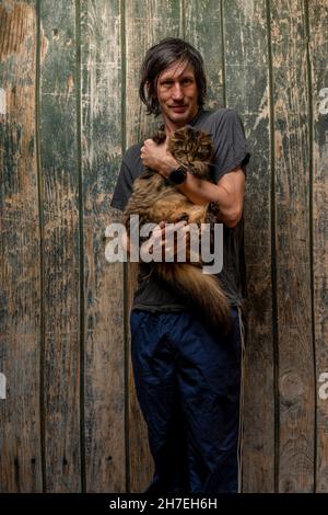 Black hair man with tabby small cat near wooden old wall Stock Photo