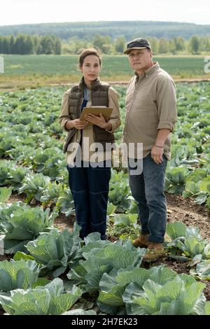 Mature and middle-aged workers of cabbage field standing on plantation and looking at camera Stock Photo