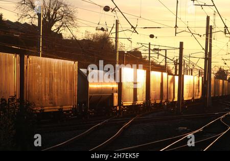 Sunset glint reflecting off containers as freight train passes through Carnforth on West Coast Main line on 22nd November 2021. Stock Photo