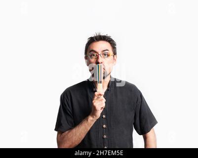 Dark-haired man in black shirt wearing glasses, covers his mouth with a closed fan with rainbow colors as a sign of silence. LGBTQ concept. Copy space Stock Photo