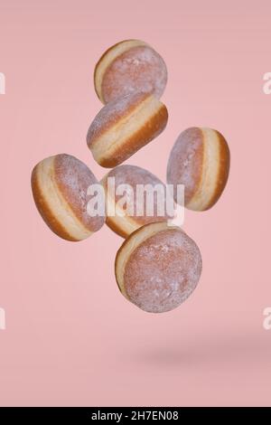 Fresh donuts sprinkled with powdered sugar flying on pastel pink background. Minimal dessert and sweet concept Stock Photo