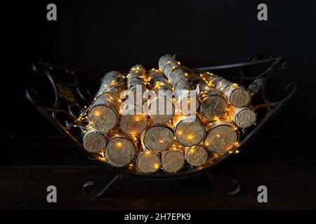 Illuminated Christmas decoration glowing in the dark. Closeup firewood in the fireplace with Christmas lights. Stock Photo