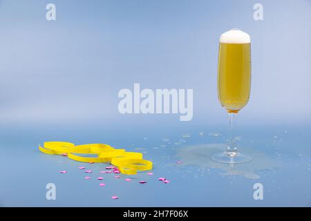 sparkling wine glass with champagne in glass against blue background, yellow streamers and confetti on table, happy new year, studio shot Stock Photo
