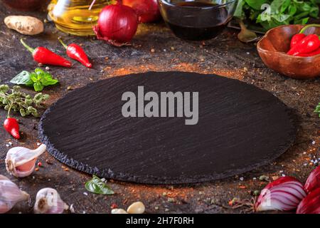 Culinary background with kitchen slate round board, olive oil in a jug and vegetables. Empty space for menu or recipe with selective focus Stock Photo