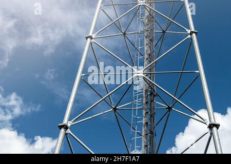 Bottom perspective pov of modern metal steel mobile 5g network wireless telecom tower against clear blue sky background on bright day. Microwave Stock Photo
