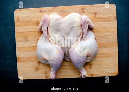 Raw Spatchcocked Chicken on a Bamboo Cutting Board: Uncooked butterflied poultry on a wooden carving board Stock Photo