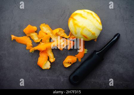 Strips of Orange Zest Next to a Whole Orange: Strips of orange peel with a vegetable peeler on a dark background Stock Photo