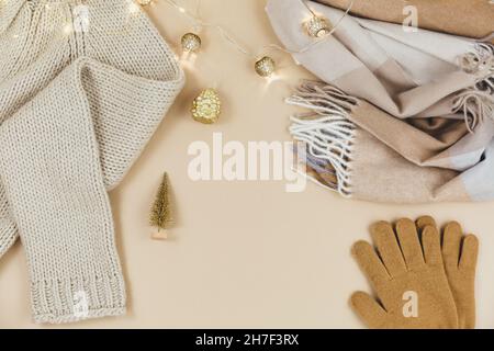Women fashion winter clothes and accessories. Female look with knitted sweater, pullover, scarf, garlands on beige pastel background. Stock Photo