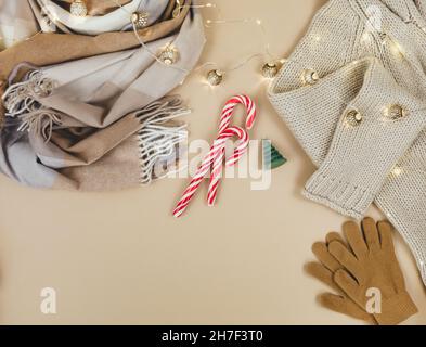 Women fashion winter clothes and accessories. Female look with knitted sweater, pullover, scarf, garlands on beige pastel background. Stock Photo