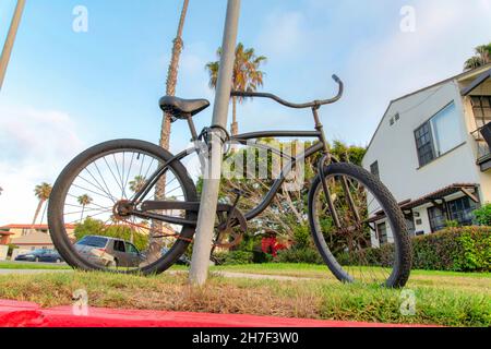 Bicycle locked on a metal pole at La Jolla, California. Parked black bicycle on a lawn with cable lock against the view of a house on the right and pa Stock Photo