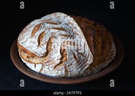Homemade round dark bread with flour crust and painted spikelet on a clay plate Stock Photo