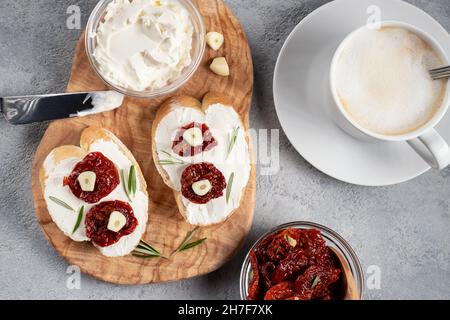 Homemade sandwiches with cream cheese and sun-dried tomatoes on a wooden board of olive - delicious healthy breakfast, italian cuisine, flat lay. Stock Photo